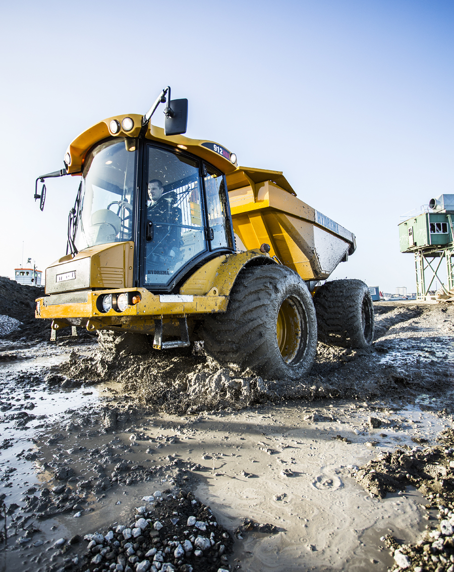 Gele Hydrema knikdumper op een modderige bouwwerf, gefotografeerd van laag standpunt tegen een heldere lucht.
