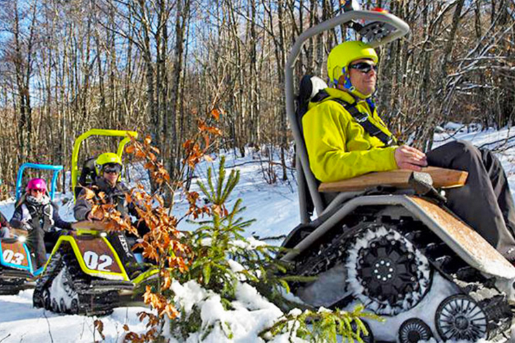 Felgroene elektrische Ziesel-rupsvoertuigen bereden door personen in groene helmen door een besneeuwd winterbos.
